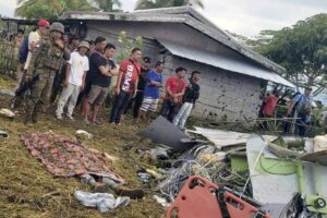 The body of a victim is covered with a blanket as members of security forces stand around wreckage of airplane in a rice field in Maguindanao del Sur province, Philippines.