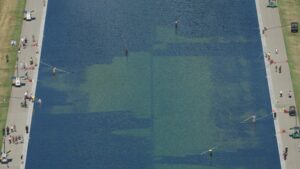 Aerial view of the Lincoln Memorial Reflecting Pool with green water, edges lined by walkways and people strolling, some fishing from the edge.