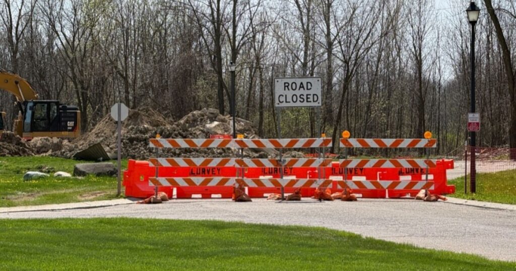 Road closed barrier with orange striped barricades and a construction site in the background, indicating road work ahead